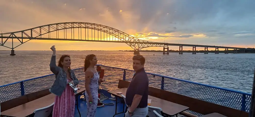 Guests on deck at sunset beneath the Robert Moses bridge